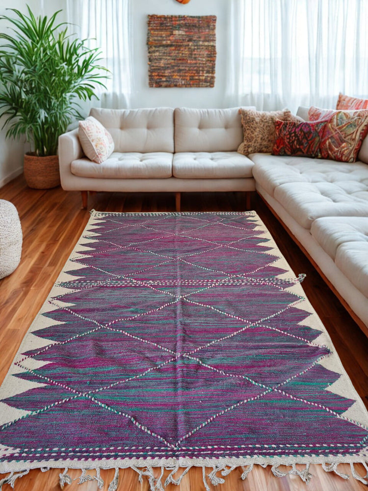 Zanafi flatweave rug in deep plum and ivory, featuring stepped triangle motifs, styled in a bright living room with neutral seating.