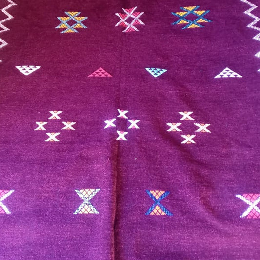 A dark purple Moroccan-style wool rug with geometric patterns and white zigzag borders, laid out on a floor.