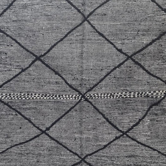 A large woven rug or textile panel with a black diamond lattice pattern on a gray and white textured base, displayed flat with fringe visible at the top and bottom edges.