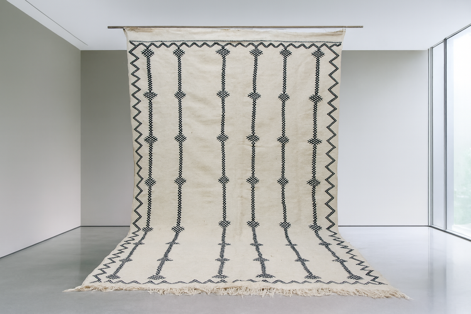 Striped Moroccan kilim rug in neutral tones, placed in a sunlit room with large windows and indoor greenery.