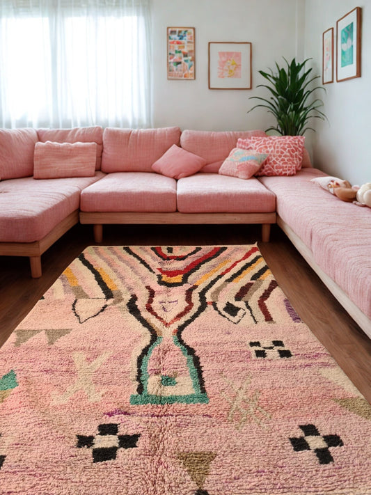 Living room with a pink sectional sofa and a patterned rug.