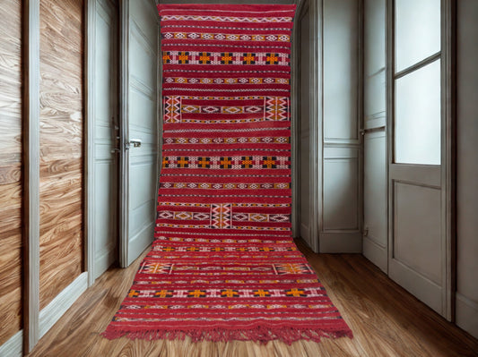 Red patterned rug on a wooden floor in a room with white walls and wooden paneling.