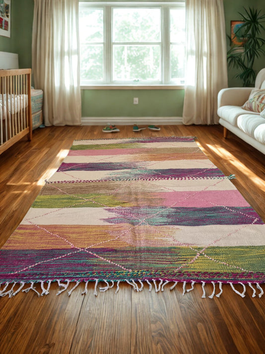 Colorful patterned rug on a wooden floor in a room with a crib and sofa.
