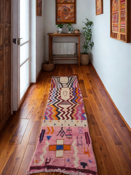 Colorful patterned rug on a wooden floor with a wooden cabinet and plants in the background.
