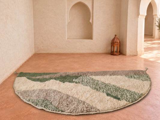 A semi-circular shag rug with abstract wavy stripes in cream, sage green, and taupe, displayed on a terracotta tiled floor in a Moroccan-style room with arched walls and a lantern.