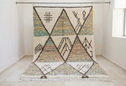 A large woven area rug with a geometric mountain pattern, hanging from a metal rod in a minimalist white room.