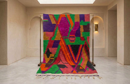 A large abstract patterned rug displayed on a black metal stand in a minimalist beige hallway with arched walls and a marble floor.