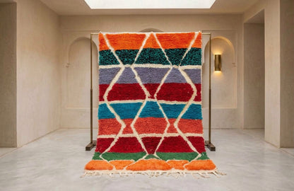A colorful Moroccan-style shag rug with a geometric diamond pattern, displayed on a metal stand in a minimalist beige room.