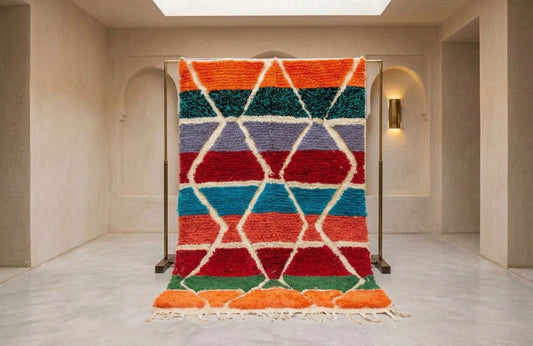 A colorful Moroccan-style shag rug with a geometric diamond pattern, displayed on a metal stand in a minimalist beige room.
