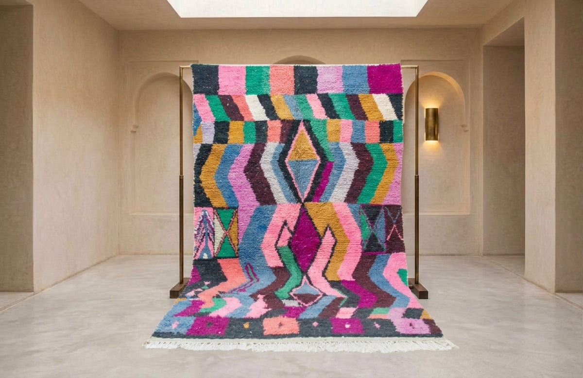 A vibrant, multicolored geometric patterned rug displayed on a wooden stand in a minimalist, warm beige interior room.