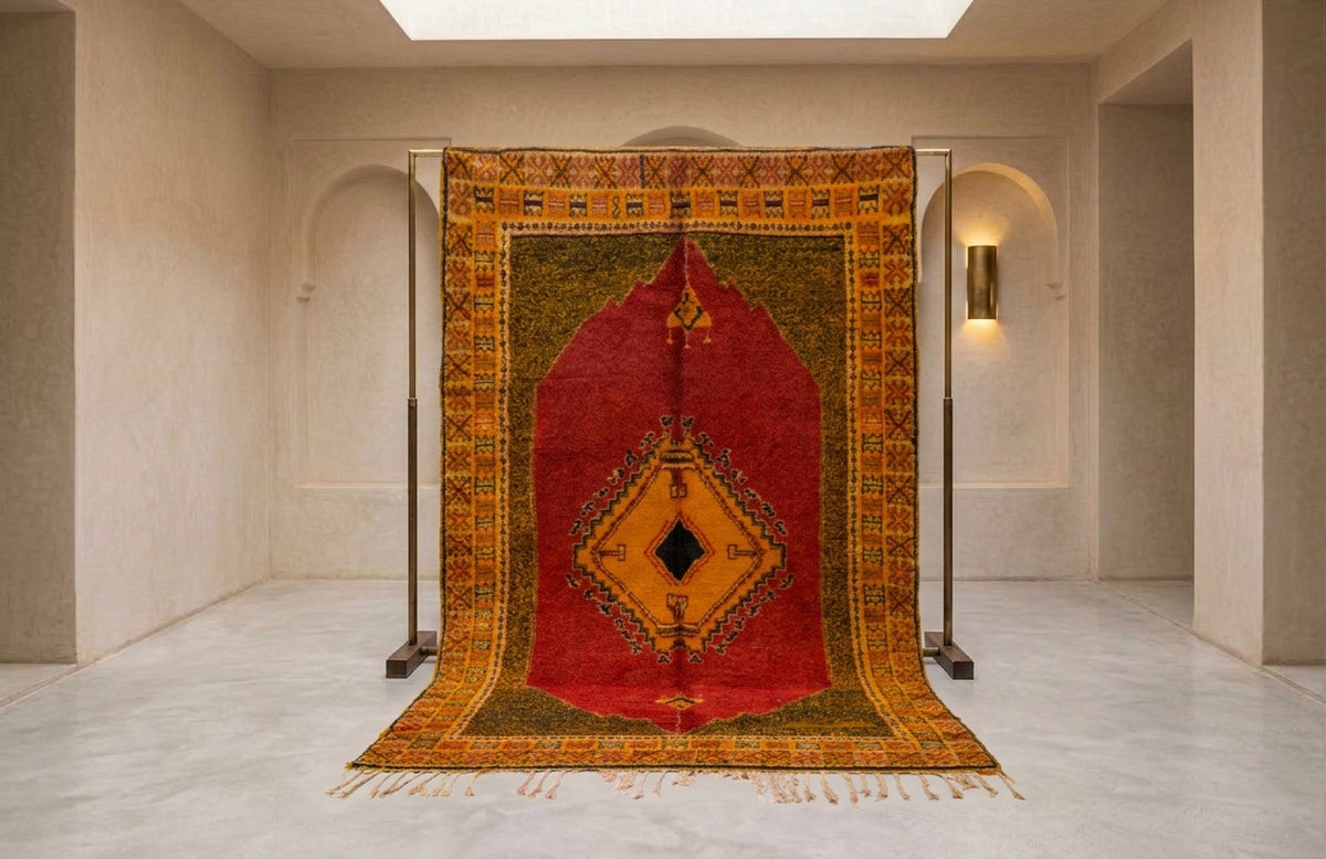 A large traditional oriental rug displayed on a metal stand in a minimalist, warm-toned gallery room with beige walls and arches.