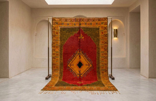A large traditional oriental rug displayed on a metal stand in a minimalist, warm-toned gallery room with beige walls and arches.