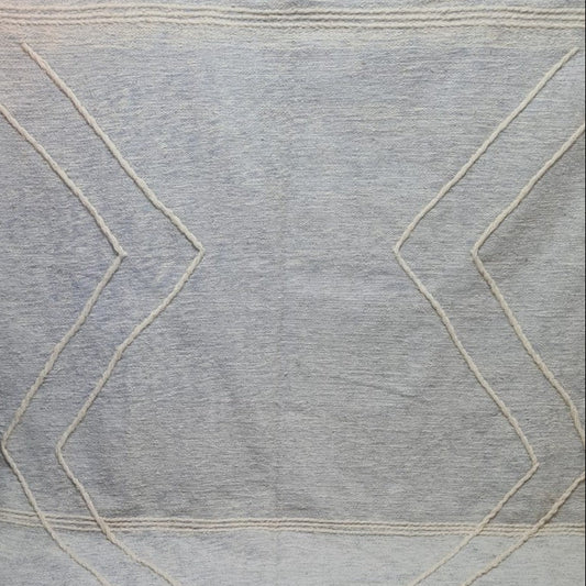 A light gray woven rug with a cream zigzag geometric pattern and fringe tassels along the bottom edge, displayed on a tiled floor.