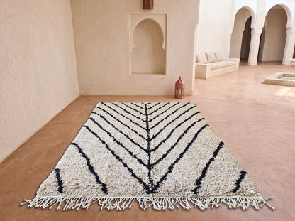 A large rectangular area rug with a cream and black chevron pattern and fringe, displayed on a terracotta floor in a Moroccan-style courtyard.