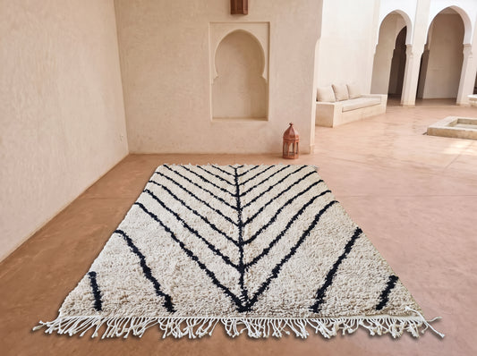 A large rectangular area rug with a cream and black chevron pattern and fringe, displayed on a terracotta floor in a Moroccan-style courtyard.