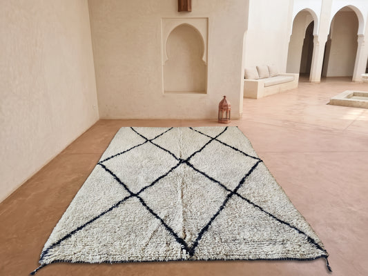 A large rectangular shag rug with a black geometric diamond pattern, displayed on a terracotta-colored floor in a minimalist Moroccan-style courtyard.