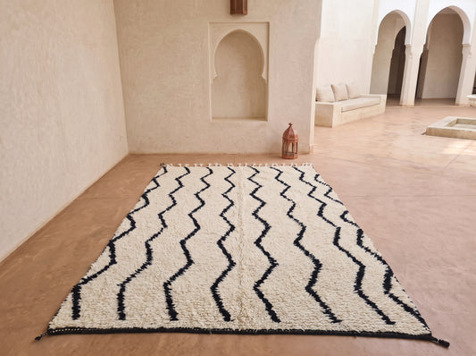 A large rectangular area rug with a black zigzag pattern on an off-white shaggy background, displayed on a terracotta-colored floor in a Moroccan-style courtyard.