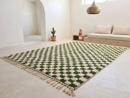 A Moroccan-style woven area rug with a green and cream geometric diamond pattern and tasseled edges, displayed in a bright, modern minimalist living room.