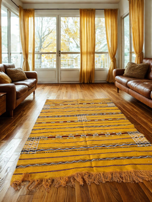 Living room with a yellow patterned rug, brown leather sofa, and large windows with yellow curtains.
