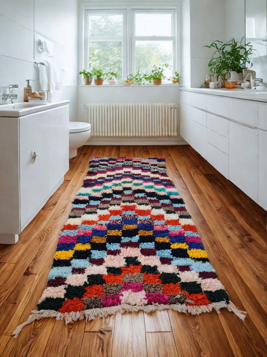 Colorful patterned rug on a wooden floor in a bathroom with white cabinets and plants.