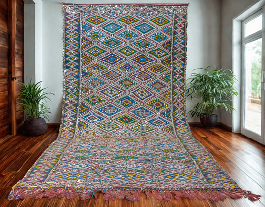 Colorful patterned rug on a wooden floor with plants and a window in the background