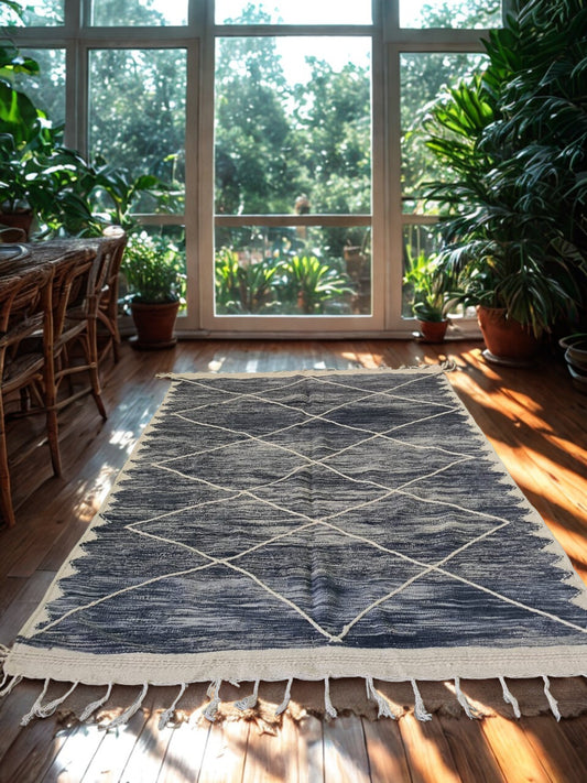 Dining room with a patterned rug on wooden floor, large windows, and potted plants.
